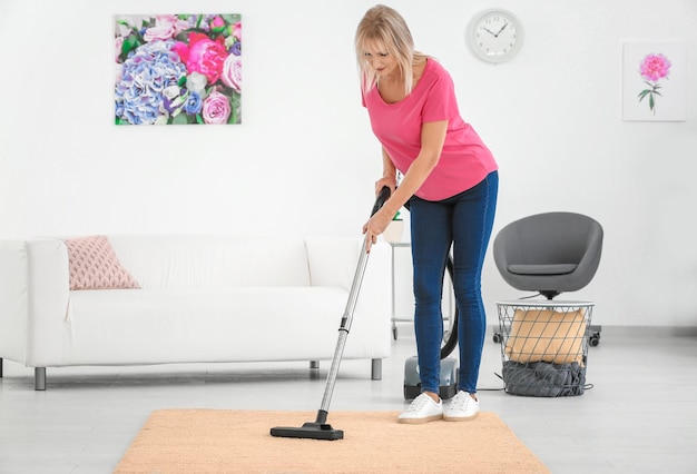 Mature woman hoovering carpet with vacuum cleaner at home