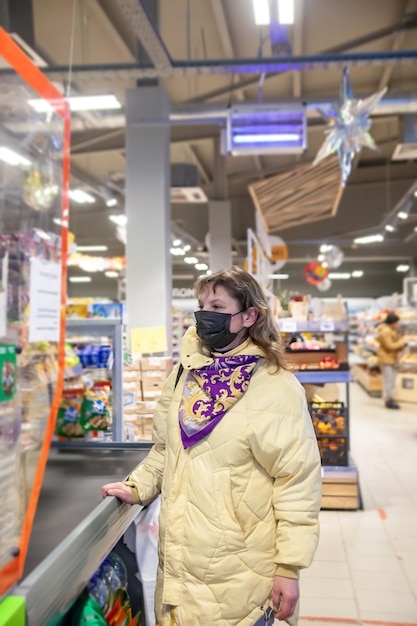 Фото Зрелая женщина в защитной маске выбирает продукты питания на полках в продуктовом магазине