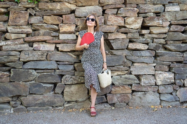 Mature woman leaning on a stone wall and fanning herself through the strong summer heat