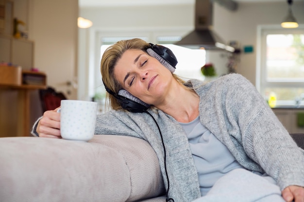 Photo mature woman listening music on headphones while resting at home