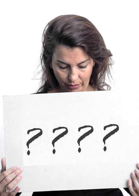 Mature woman looking at question marks on placard against white background