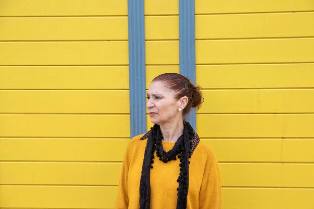 Mature woman looking to the side. In the background a colored wooden shed.