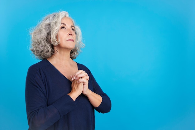 Mature woman looking up while praying with folded hands