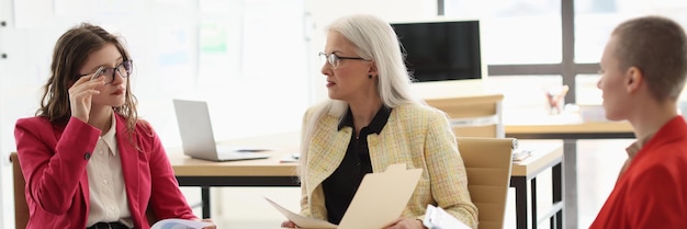 Mature woman manager discusses working details with employees sitting on chairs in office