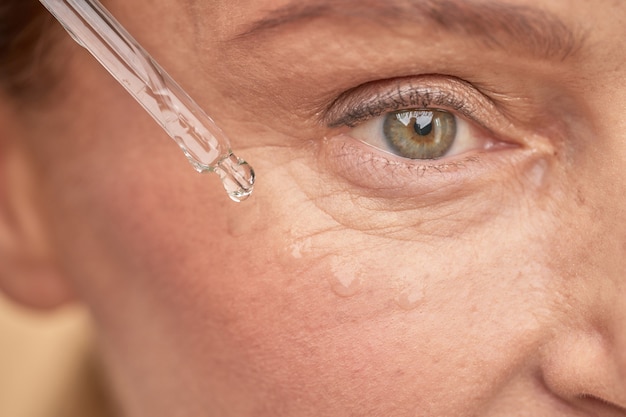 Mature woman moisturizing the skin near the eyes with a special serum