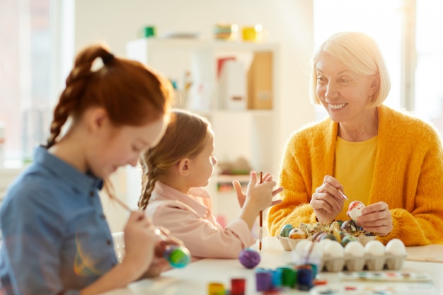 Photo mature woman painting eggs for easter