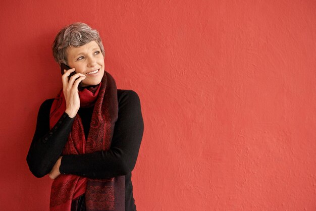 Foto donna matura telefonata e sorriso vicino al muro con spazio per la comunicazione mockup e ascolta su sfondo rosso smartphone donna senior e pensa all'idea in mock up per chattare in rete e parlare