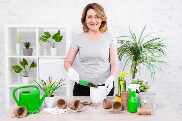 Mature woman planting flowers in pots at home