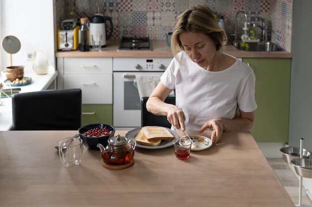 Фото Зрелая женщина готовит завтрак, намазывая тосты с маслом для чаепития на уютной кухне