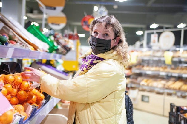 Зрелая женщина в защитной маске выбирает продукты на полках в продуктовом магазине