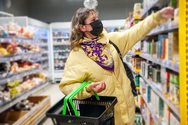 Foto donna matura in maschera protettiva che sceglie prodotti alimentari sugli scaffali del negozio di alimentari