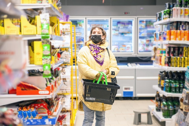 Mature woman in protective mask choosing food products on shelves in grocery shop