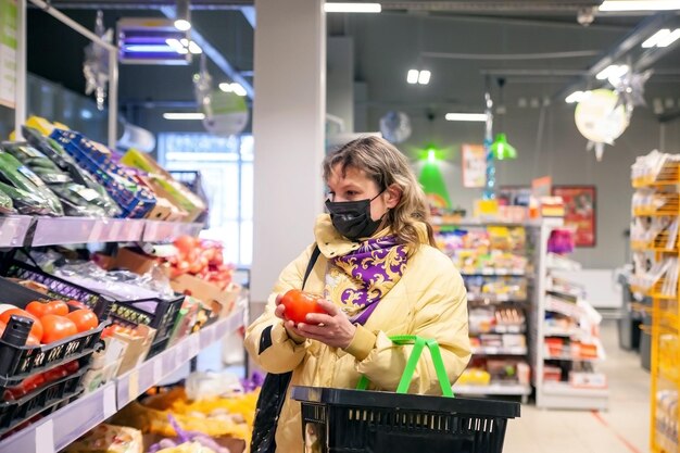 Зрелая женщина в защитной маске выбирает продукты на полках в продуктовом магазине