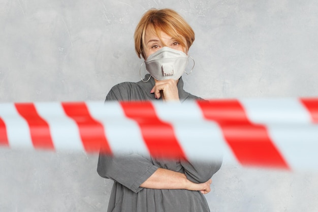 Foto donna matura con maschera protettiva su sfondo grigio con nastro di avvertimento