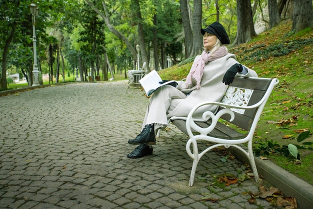 Зрелая женщина читает книгу и играет в осеннем парке. Свободное время.