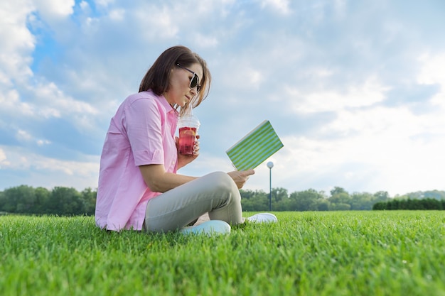 Mature woman reading book with drink