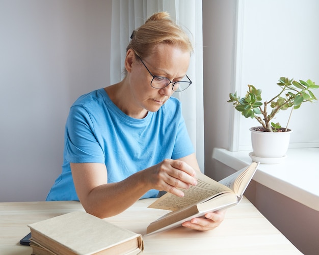 Зрелая женщина читает в очках книгу, листает страницы, пенсионерка учится, получает новые знания