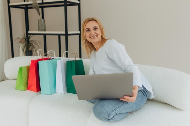 Mature woman shopping online at home on laptop Woman makes an order online Attractive woman with shopping bags Online shopping concept