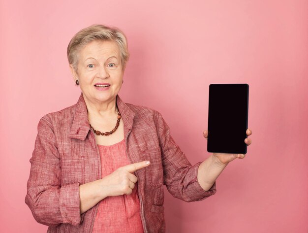 Mature woman showing a tablet computer and smiling on pink background