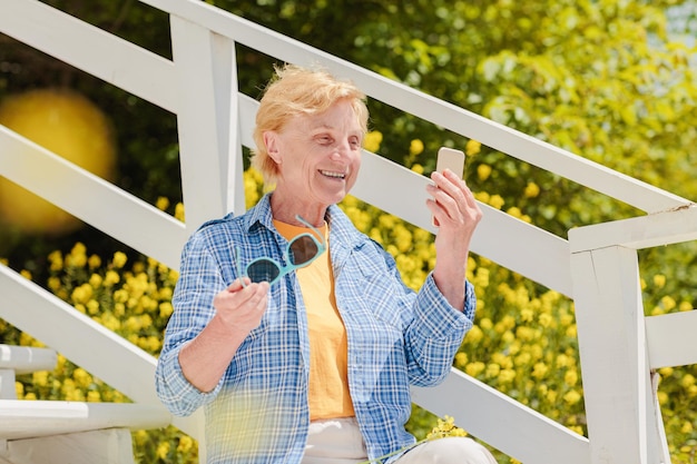 Mature woman sitting alone on the terrace of beach cafe and using mobile phone