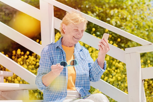 Mature woman sitting alone on the terrace of beach cafe and using mobile phone