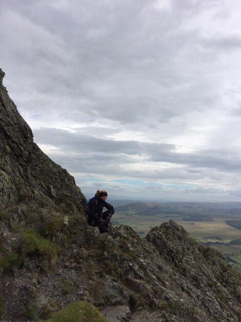 Mature woman sitting on mountain against cloudy sky