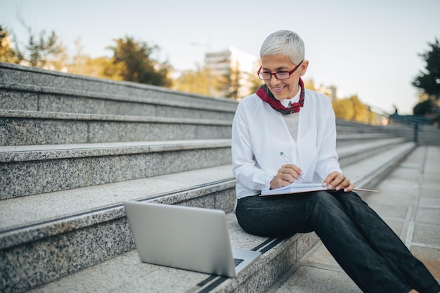 Mature woman sitting outdoors with her computer