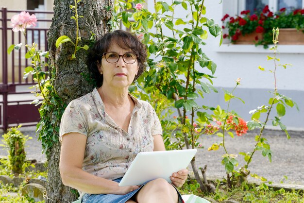 Зрелая женщина сидит с планшетом в саду