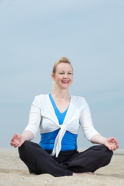 Mature woman sitting in yoga position at beach