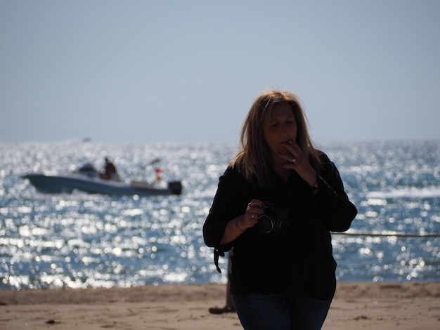 Mature woman smoking cigarette while standing against sea at beach