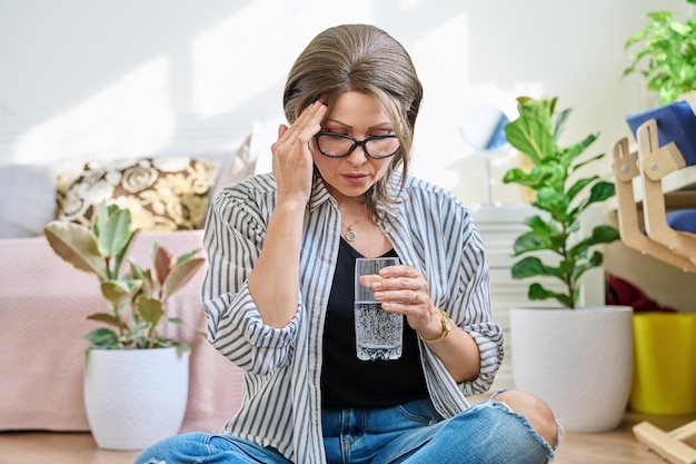 Mature woman suffering from headache at home with a glass of water
