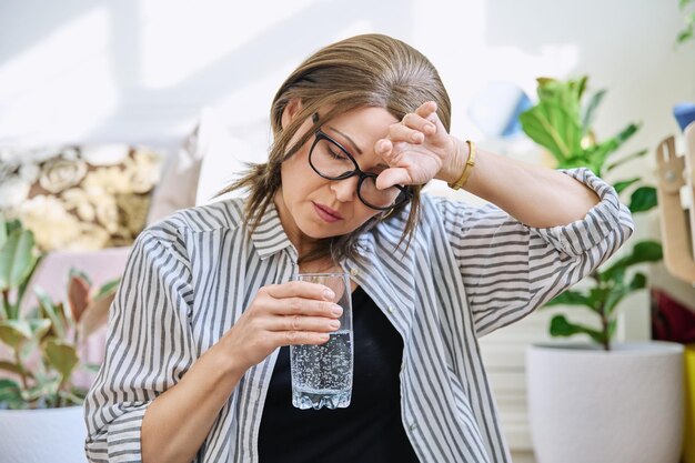 Photo mature woman suffering from headache at home with glass of water