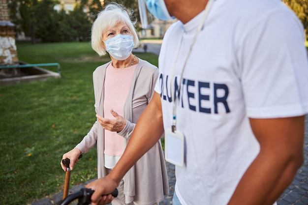 Mature woman supporting herself with a walking stick while taking a stroll with a young person