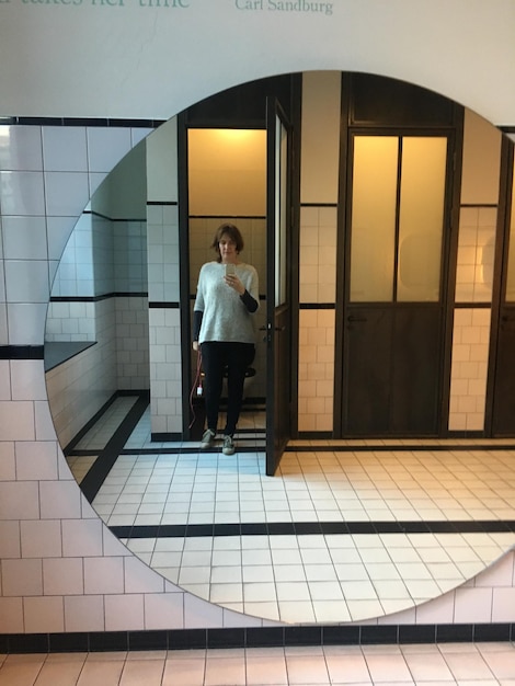 Photo mature woman taking selfie with mobile phone reflecting on mirror in bathroom