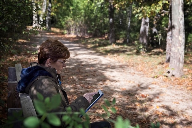 Foto donna matura che usa un tablet digitale mentre è seduta su una panchina al parco