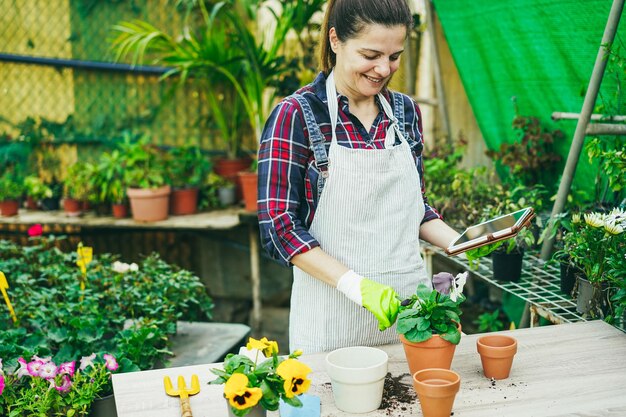 写真 温室の庭内でタブレット コンピューターを使用する成熟した女性の顔に焦点を当てる