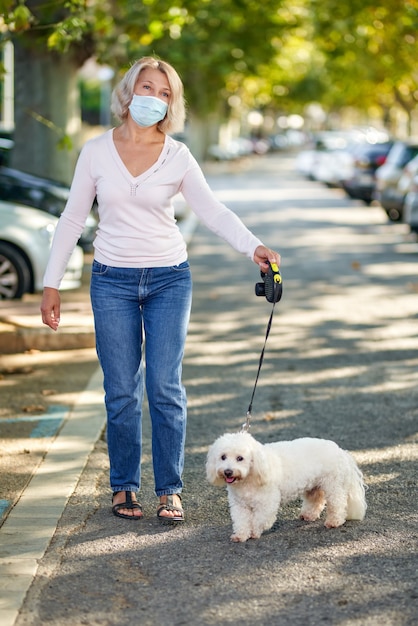Зрелая женщина гуляет с собакой на открытом воздухе в антивирусной маске