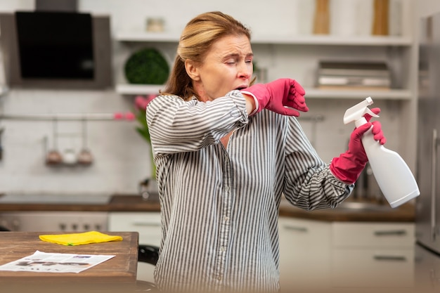 Mature woman wearing protective gloves sneezing and coughing because of allergy