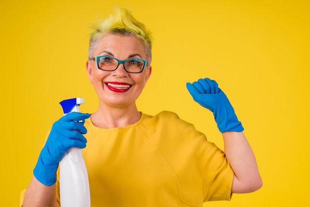 Photo mature woman with colored stylish yellow dyed hair in warm dress washing floor at home background studio copy spase.