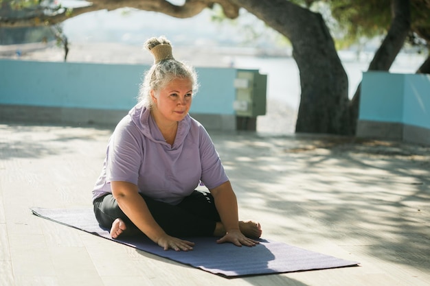 Mature woman with dreadlocks working out doing yoga exercises on sea beach wellness wellbeing and active elderly age concept