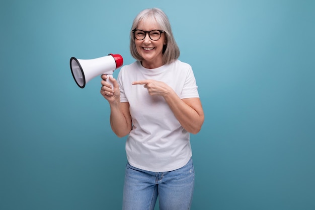 A mature woman with gray hair speaks using a megaphone on a studio background