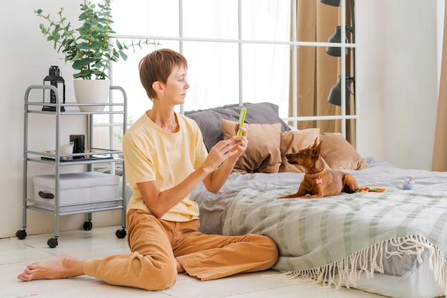 Donna matura con un telefono in mano con un pinscher pigmeo in camera da letto