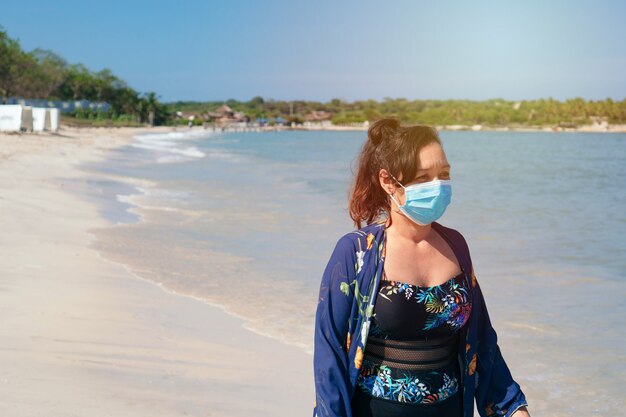 Mature woman with protective mask walks on the beach