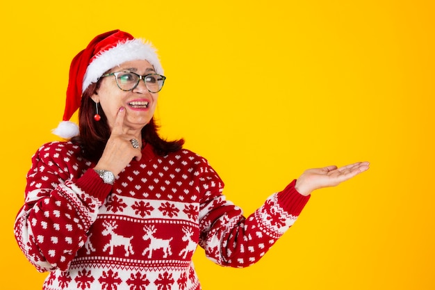 Mature woman with santa claus hat happy pointing copy space yellow background