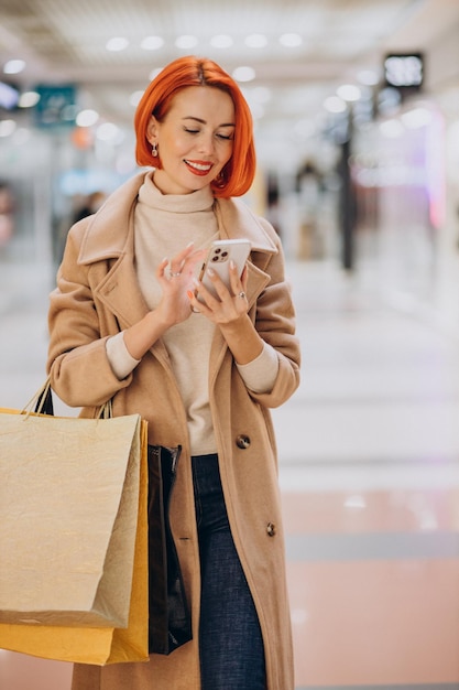 mature woman with shopping bags in mall using phone