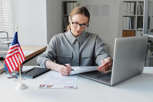 Mature woman working in us embassy sitting at desk in office\
looking through data in visa applicatio