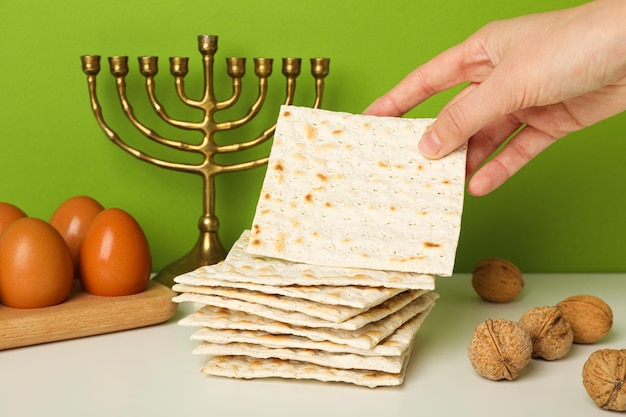 Matzo in de hand noten eieren op houten steun en hanukkiah op groene achtergrond