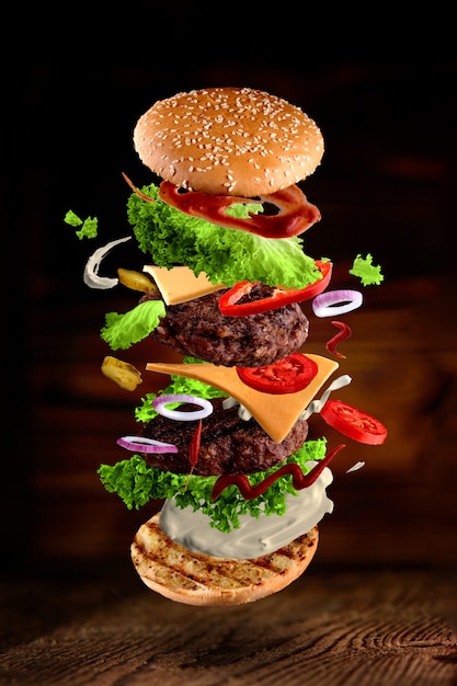 Maxi hamburger, double cheeseburger with flying ingredients isolated on wooden