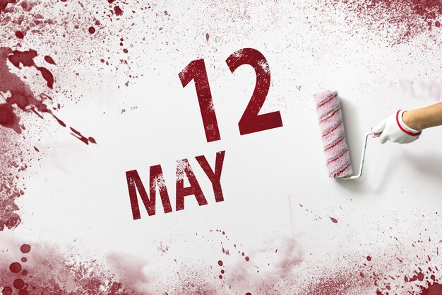 May 12nd. day 12 of month, calendar date. the hand holds a\
roller with red paint and writes a calendar date on a white\
background. spring month, day of the year concept.