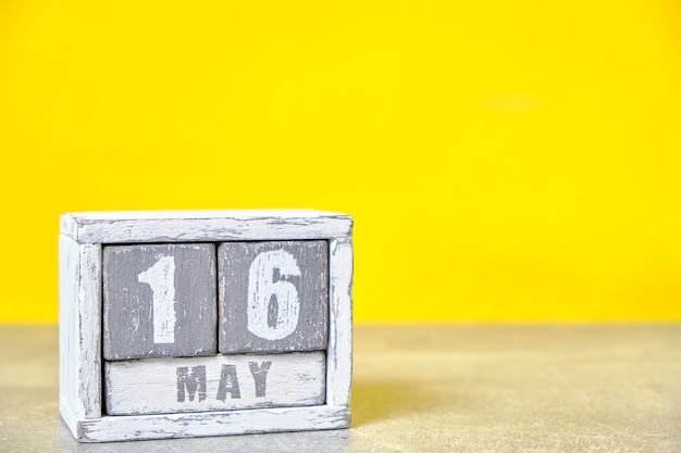 Фото Календарь на 16 мая из деревянных кубиков на желтом фоне с пустым местом для текста